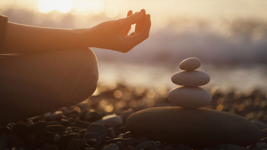 person doing yoga next to a pile of stones